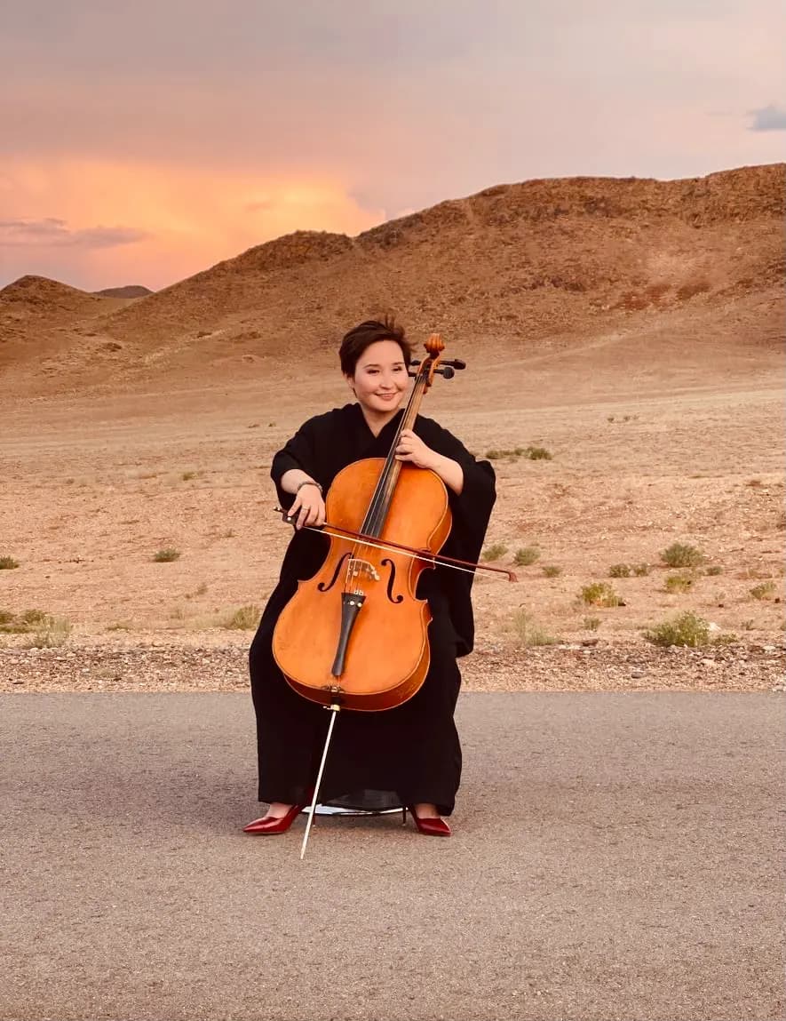 Sandi et son violoncelle devant un paysage désertique au soleil couchant